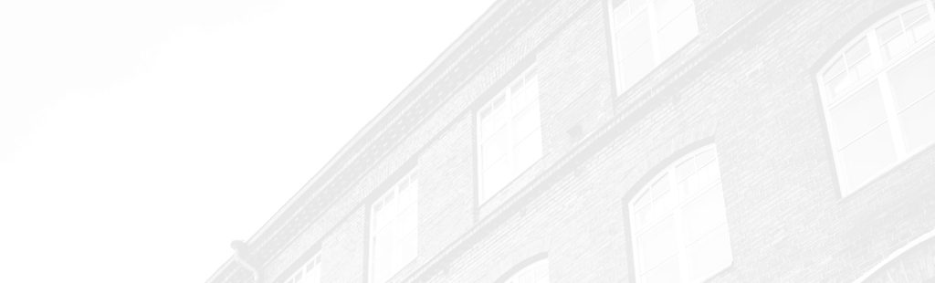 A faded, partial view of a brick building with several large windows, positioned diagonally across a white background.
